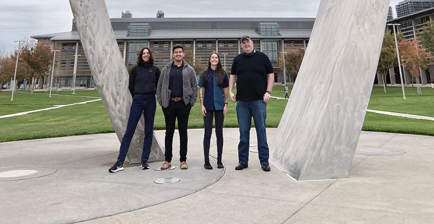 Graduate students stand before the Beginnings sculpture.